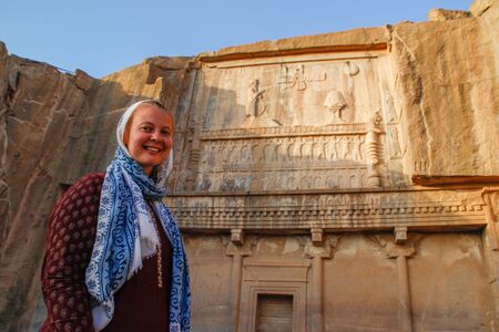 White young woman tourist with a head covered stands on the background of the famous bas-reliefs of...