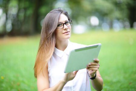 Young woman, girl working with tablet and phone in green field, park with sunshine
