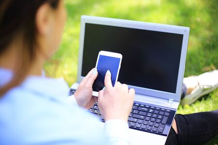 A young attractive woman studying outside with phone and laptop