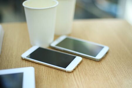 Two white mobile phones with tablet on wooden table background, blank screen electronic device with copy spaceの写真素材