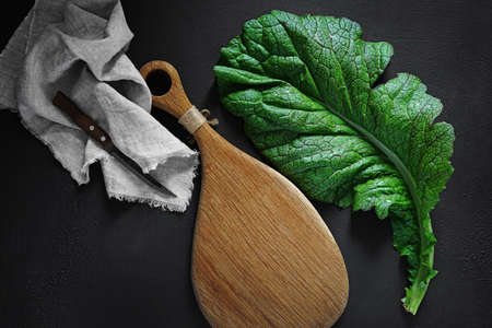 green big leaf of japanese mustard mizuna on a dark background with cutting board , top view. Useful...