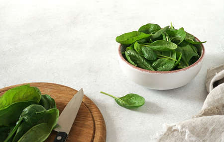 Fresh spinach leaves with water drops in ceramic bowl and cutting desk on the light background. Selective focus. Space for text.の写真素材