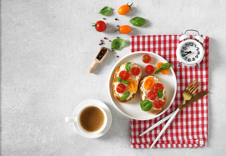 Breakfast sandwiches with cheese and tomatoes. a cup of coffee and alarm clock. Bruschetta or...