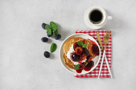 Pancakes with caramelized plums with mint leaves and cup of coffee. top view, copy space. morning breakfast conceptの写真素材