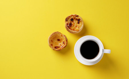 Pastel de nata on yellow background with cup of coffee. Top view, copy space