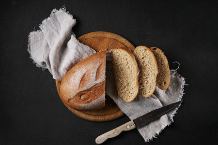 Fresh homemade bread cutting into slices on wooden board with napkin, top view