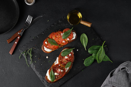 Delicious toasted bread with tomatoes, feta cheese, spinach and herbs on black board, close upの写真素材