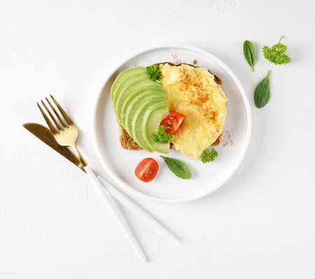 Omelette with tomato and avocado on bread on white plate, light background, top viewの写真素材