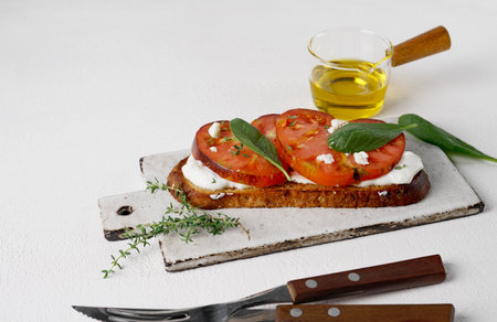 Delicious toasted bread with tomatoes, feta cheese, spinach and herbs on light boardの写真素材