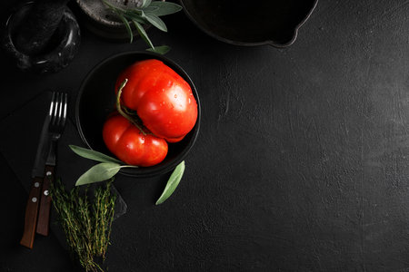 Big red tomato in black bowl on black background. top view, copy spaceの写真素材
