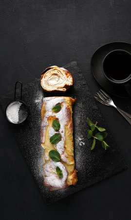 Finnish pancake pannukakku rolled up and filled with cream on a black board on a black background with cup of tea. tasty breakfast, top vertical view, copy spaceの写真素材