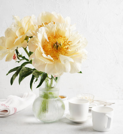 Creamy peonies in vase and cups for tea on white table in morning lights, copy spaceの写真素材
