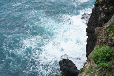 A cliff overlooks the ocean, with waves crashing against its surface