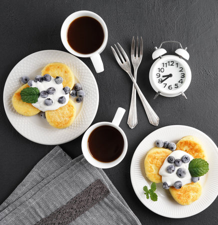 syrniki . Appetizing cheesecakes with sauce and frozen blueberries and cups of coffee on black table. Breakfast concept, top viewの写真素材