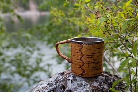 A steel mug with birch bark trim stands on the rock.