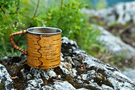 A steel mug with birch bark trim stands on the rock.の写真素材