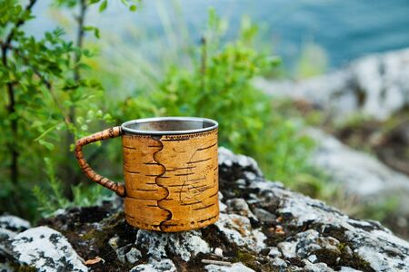 A steel mug with birch bark trim stands on the rocks.の写真素材