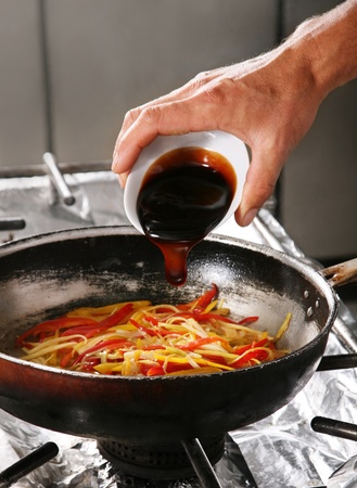 Chief adds sauce in fried pepper on professional kitchenの写真素材