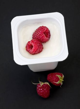 Sweet raspberry fruit closeup in milk yogurt on blackの写真素材