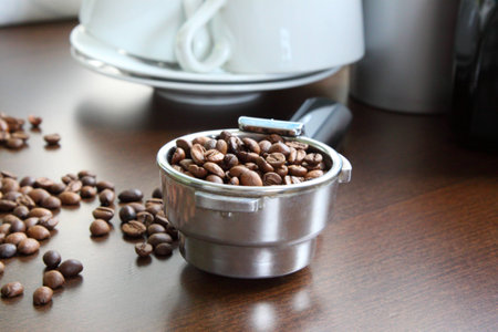 Coffee grains in a measured, metal spoon. Against ware and subjects of kitchen which are visible...