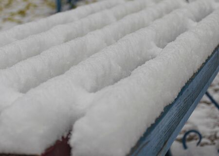 Wooden blue park bench covered by snow. The first snow in the city. Cloudy snowy weather.の写真素材