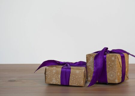Gifts packed in craft paper and tied with satin ribbon on a wooden background.の写真素材
