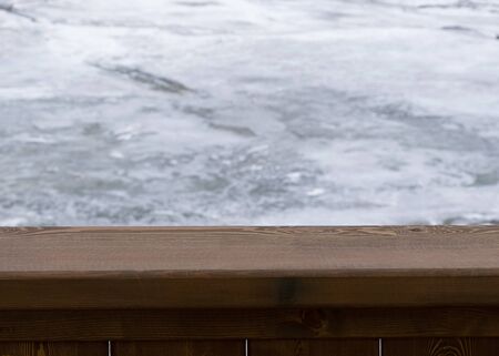 Brown wooden board with blurry winter background of a frozen river. Cold weather. Wood surface for design.の写真素材