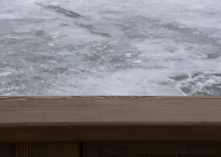 Brown wooden board with blurry winter background of a frozen river. Cold weather. Wood surface for design.の写真素材