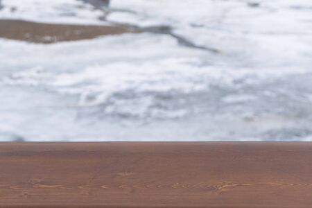 Brown wooden board with blurry winter background of a frozen river. Cold weather. Wood surface for design.の写真素材