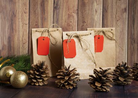 Vintage handmade gift boxes made of kraft paper on a wooden background in the Christmas style, decorated with golden Christmas balls, cones, fir branch. Christmas, New Year, winter holiday. Kraft package, holiday concept, top view, flat lay. Mocap.の写真素材