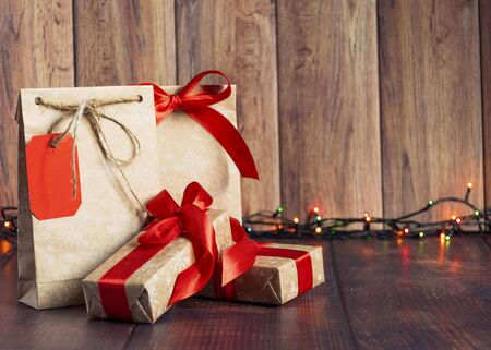 Gift bag made of handmade kraft paper on a wooden background in a Christmas style, decorated with Christmas tree balls, cones, a ball of rope, fir branches. Christmas, New Year, winter holiday. Kraft package, holiday concept, top view, flat lay.Mocap.の写真素材