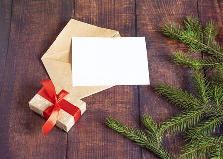 Blank white paper card in a brown envelope from handmade craft paper on an old wooden table in a Christmas style. Fir branches, cones on the table. Christmas and New Year.の写真素材