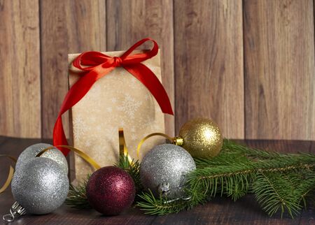 Gift bag made of handmade kraft paper on a wooden background in a Christmas style, decorated with Christmas tree balls, cones, a ball of rope, fir branches. Christmas, New Year, winter holiday. Kraft package, holiday concept, top view, flat lay.Mocap.の写真素材