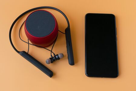 Wireless bluetooth devices for the phone, black headphones and a red speaker. Headset for phone on an orange backgroundの写真素材
