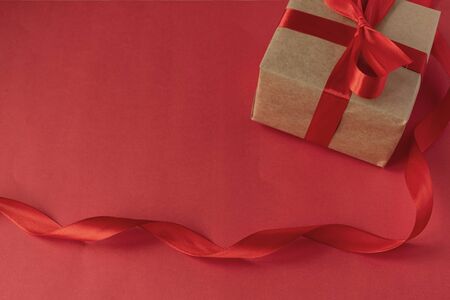 A gift for your beloved on Valentine's Day. DIY gift from kraft paper with a red satin ribbon on a red background. Birthday. March 8.の写真素材