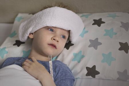 Sick sad child in temperature and headache lies in bed. Flu colds disease virus bacteriumの写真素材