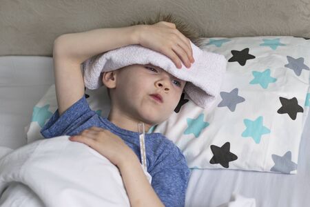 Sick sad child in temperature and headache lies in bed. Flu colds disease virus bacteriumの写真素材