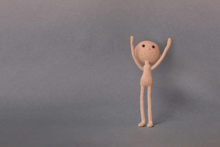 A toy man on a gray background with copy space. Cute amigurumi. Presentation  Keynote. Motivational phrase. A man holds object in his hands over his headの写真素材
