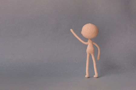 A toy man on a gray background with copy space. Cute amigurumi. Presentation Keynote. Motivational phrase. The man stands with his back and presses on the object on the leftの写真素材