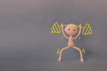 A toy man on a gray background with copy space.  Motivational phrase. A sketch is drawn on top of the photo.Man holding a barbell. Overcoming difficultiesの写真素材