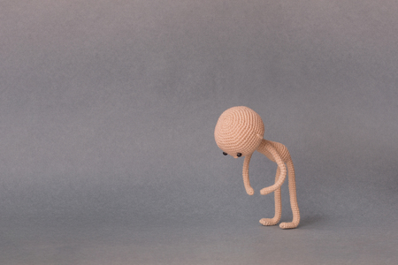 A toy man on a gray background with copy space. Cute amigurumi. Motivational phrase. Man leaned against the earth and holds the object.の写真素材