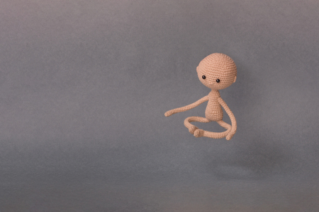 A toy man on a gray background with copy space. Cute amigurumi.  Motivational phrase. The man sits cross-legged and moves towards usの写真素材