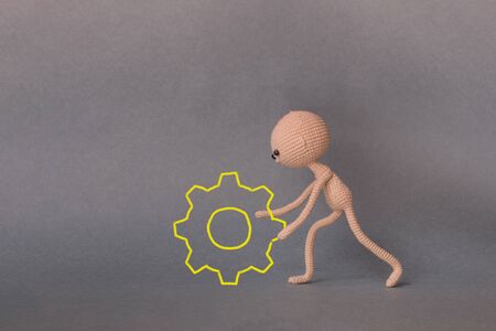 A toy man on a gray background with copy space. Presentation Keynote. Motivational phrase. A sketch is drawn on top of the photo.Man rolls a large gear in the overall mechanism.の写真素材