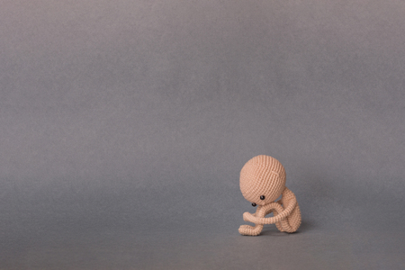 A toy man on a gray background with copy space. Cute amigurumi. Presentation Keynote. Motivational phrase. A person sits, holding his feet with his hands, sad or cryingの写真素材