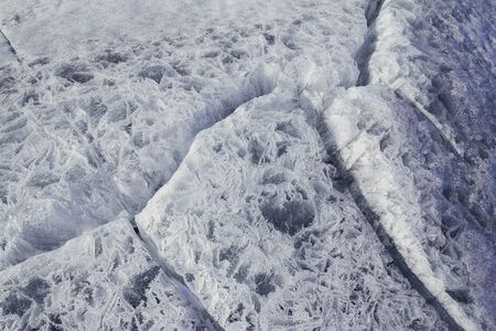 Danger on the show surface: cracks in blue ice of cracked glacier in textured white snow surface...