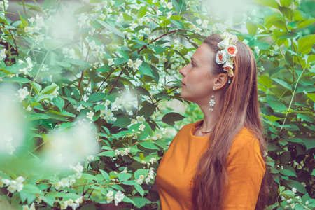 Smiling pretty young woman with long light brown hair wearing a decorative floral headband is looking down away. Portrait of a natural girl without makeup is enjoying the smell in blooming garden.の写真素材