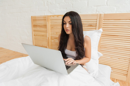 Young woman in sleepwear using laptop in bedの写真素材