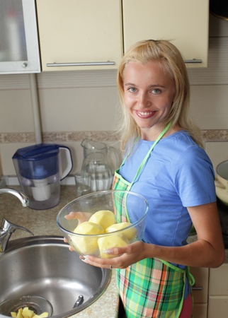 Beautiful woman cleans a potato on kitchenの写真素材