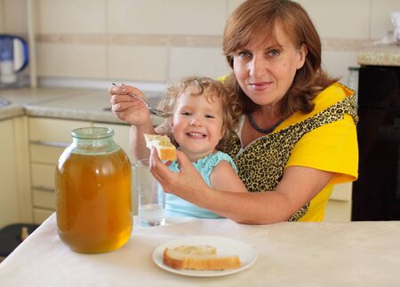 Happiness grandmother with the granddaughter eating honey with breadの写真素材