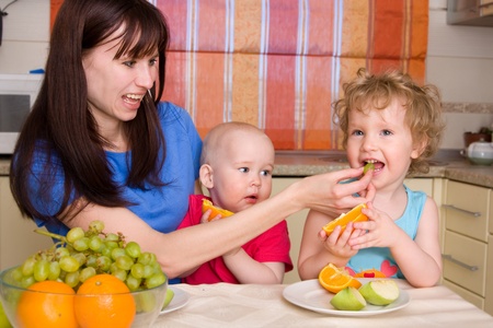Beautiful happy mum with children eat fruiton kitchenの写真素材